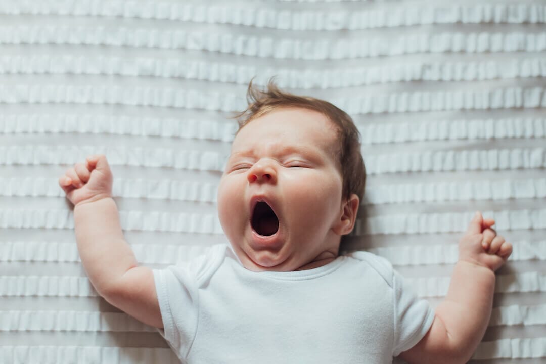 A baby yawning in bed.